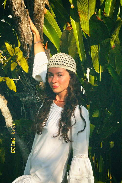 AZURE, singer and songwriter poses in tropical foliage with a white dress and knit cap.